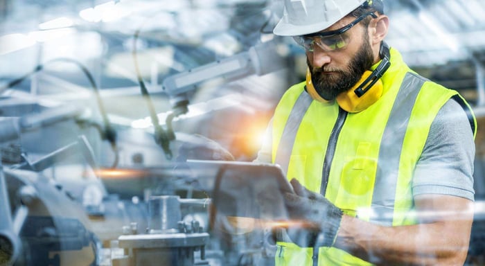Engineer in a hard hat and safety vest using a tablet in a factory